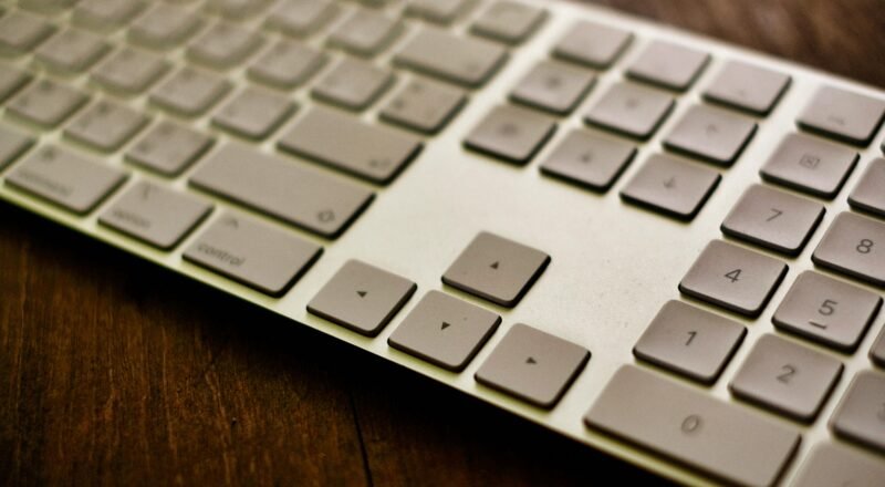 Stylized close-up of a modern white keyboard placed on a wooden desk.